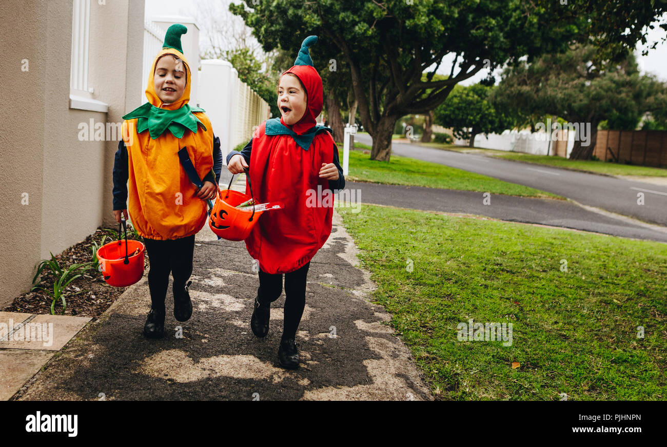 Identische Zwillingsschwestern in halloween kostüm mit halloween Eimer laufen auf dem Bürgersteig. Halloween Kinder Süßes oder Saures. Stockfoto
