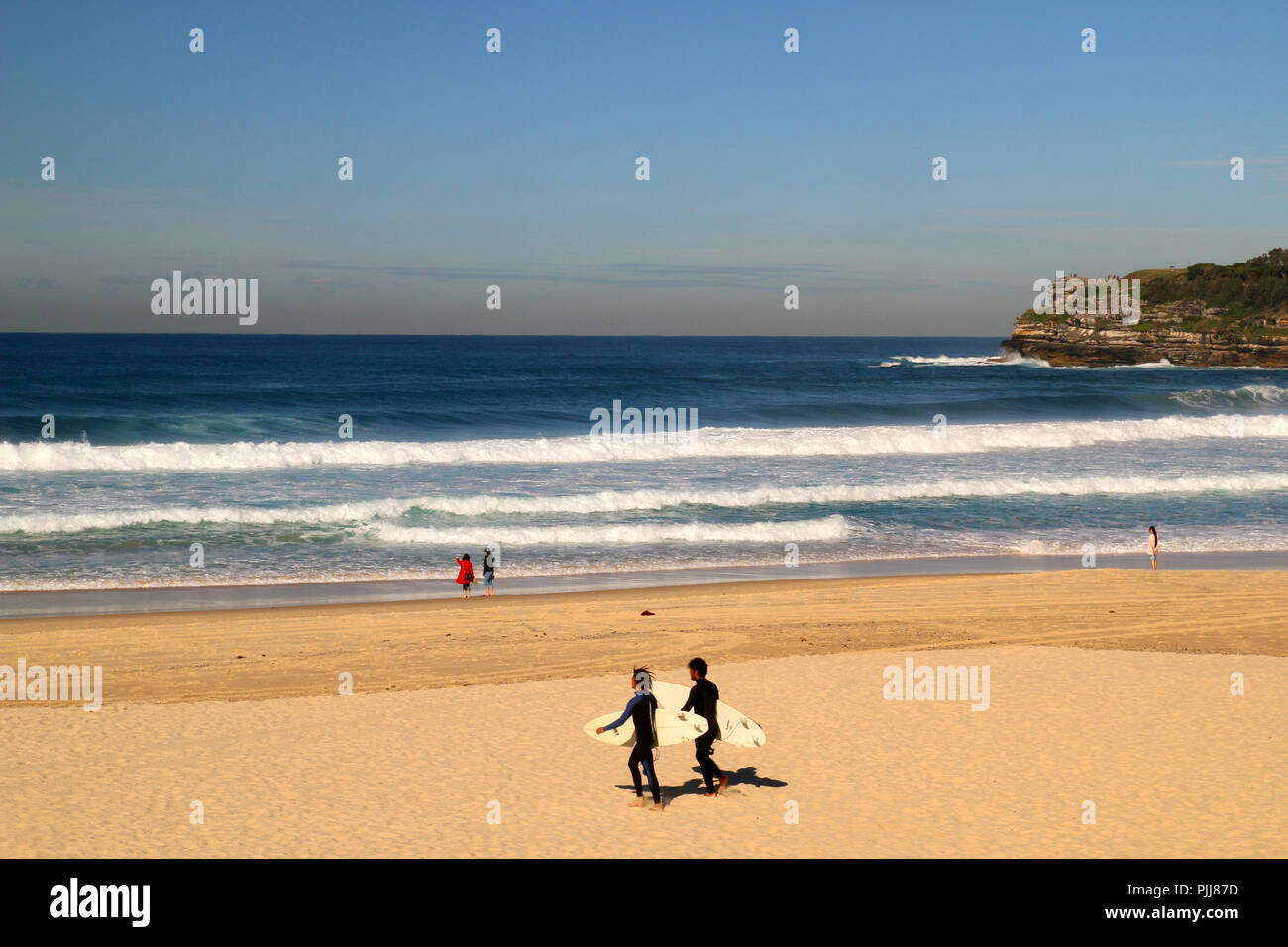 Natürliche Sandstrand in Sydney, riesige Wellen und zwei Surfer gehen mit ihren Surf zum Wasser, Pazifischer Ozean, Bondi Beach in Australien Stockfoto