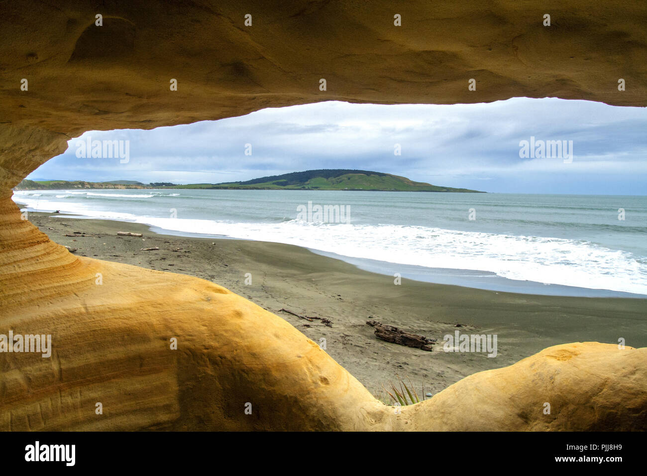 Blick von der Höhle in der Klippe auf den Gemstone Strand und Pahia Hügel, natürliche Fenster von alten Schutz in surrealen Formen der Klippen Höhlen, die Catlins Stockfoto