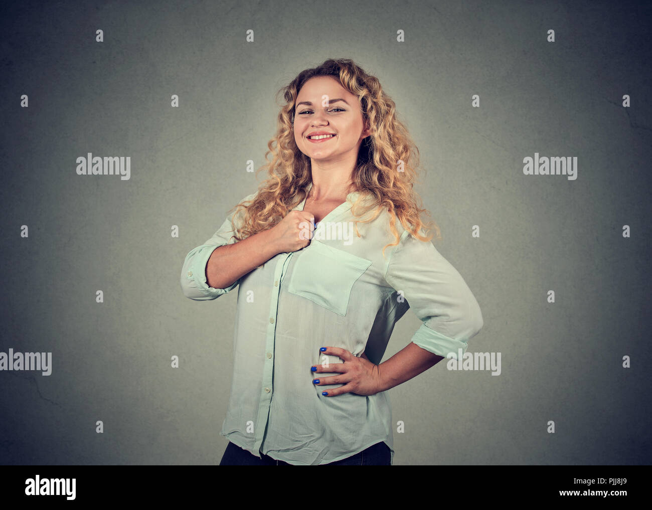 Moderne junge Frau mit der Hand auf der Brust in Stolz auf grauem Hintergrund Stockfoto