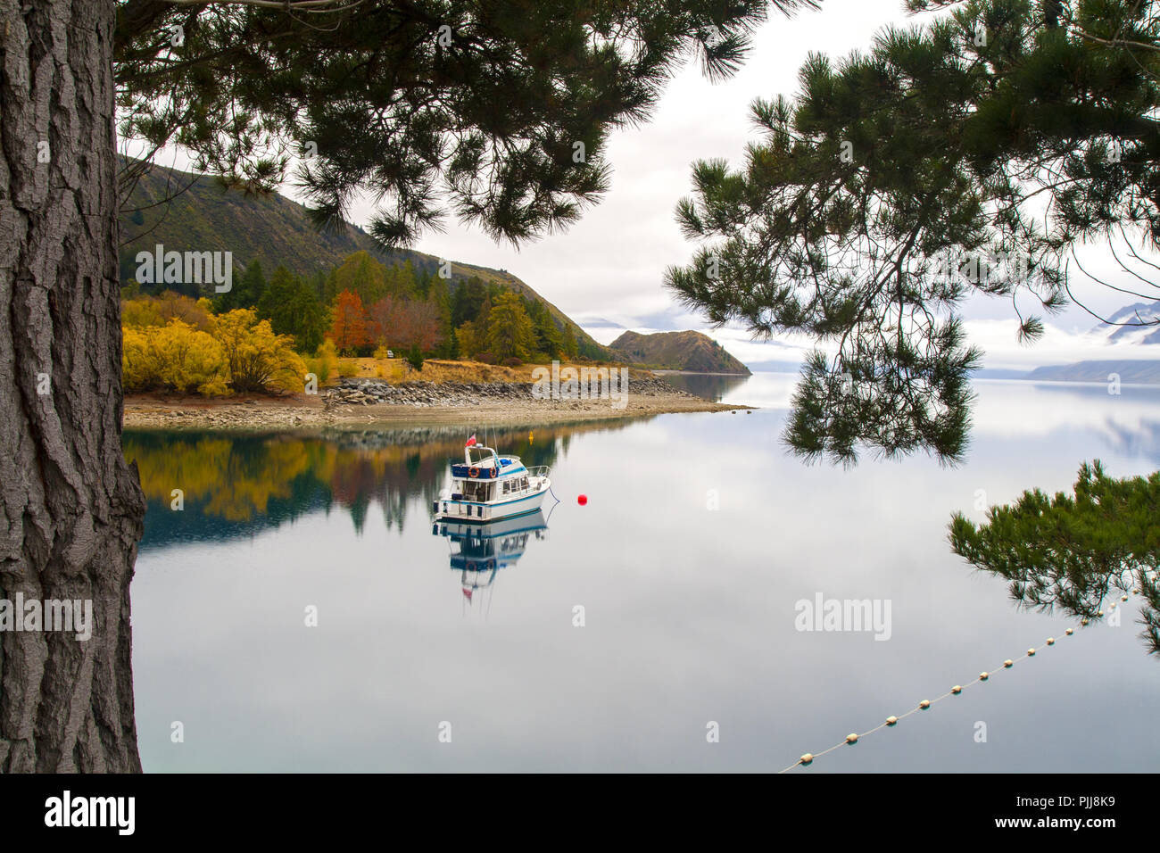 Ruhigen Herbst Landschaft mit einsamen Urlaub Boot auf dem ruhigen Wasser des unberührten Bergsee, Spiegel Wasser Reflexion, Lake Hawea, Neuseeland Stockfoto