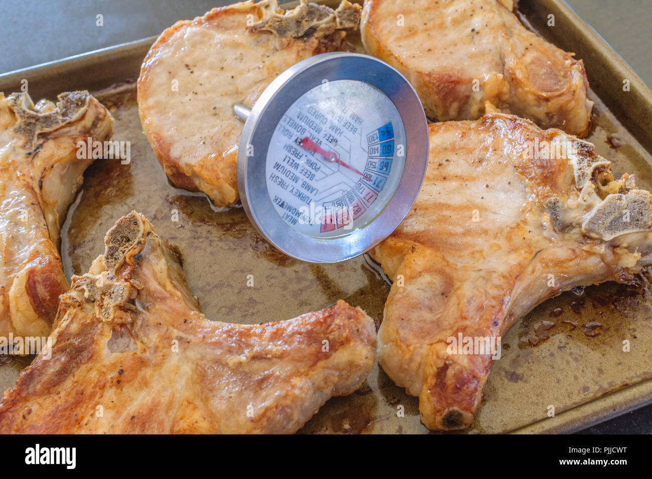 Fleisch Thermometer die Temperatur von dicken Schweinekoteletts heiß nach dem Backen auf einem Backblech Stockfoto