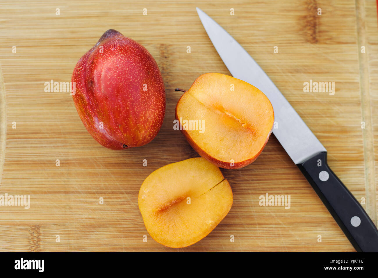 Eine volle pluot neben einem aufgeschnittenen Amigo pluot und ein Messer Stockfoto