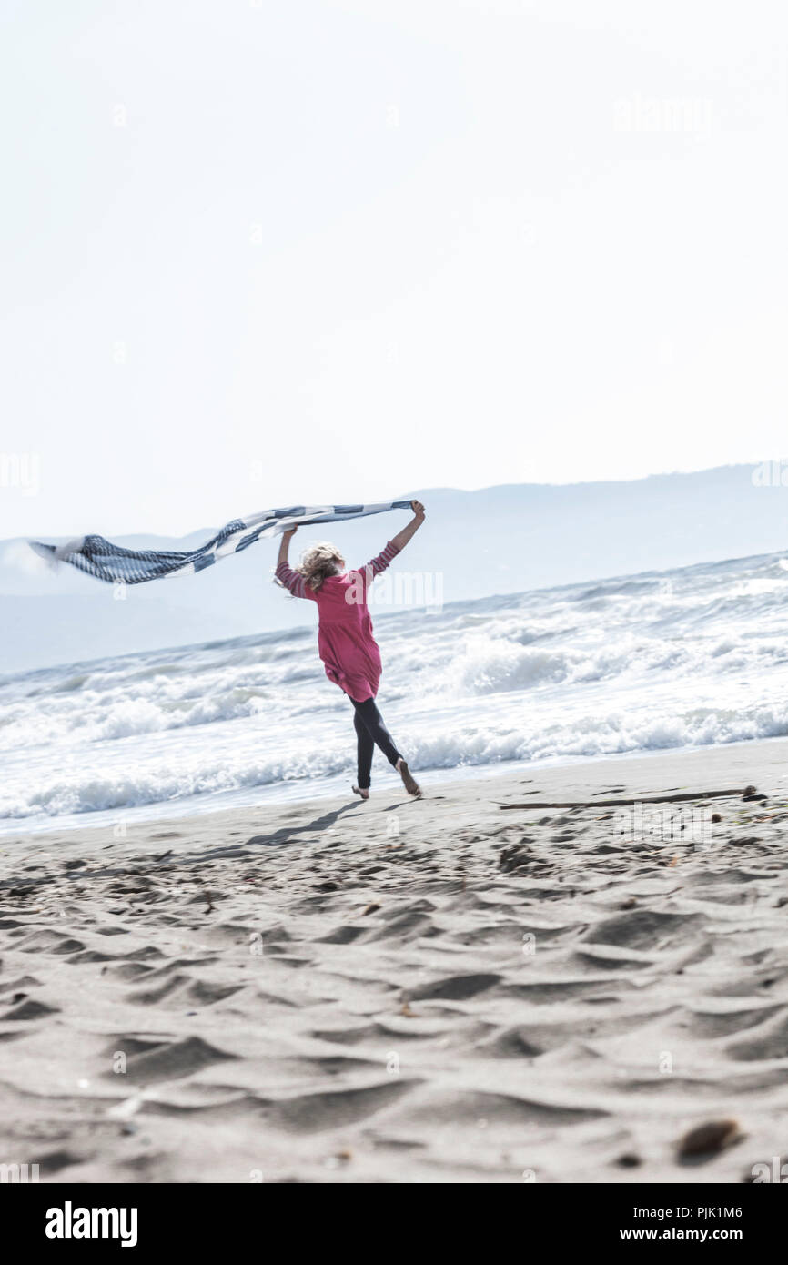 Mädchen läuft mit Handtuch am Strand Stockfoto