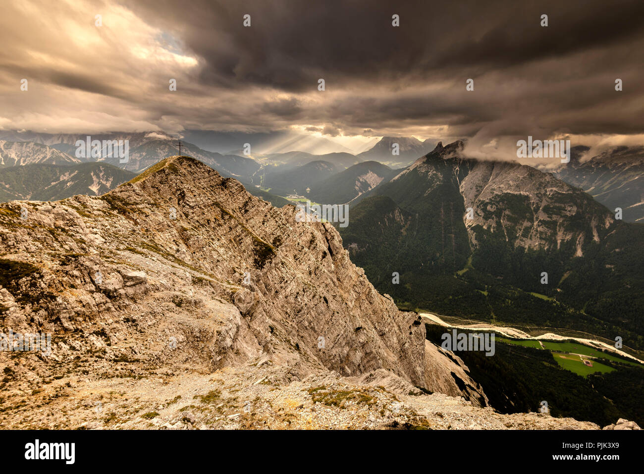 Gipfel der Brunnsteinspitze (2179 m) mit Gipfelkreuz und im Hintergrund Licht Stimmung in Tirol, von dramatischen Cloud Atmosphäre gerahmt, Stockfoto