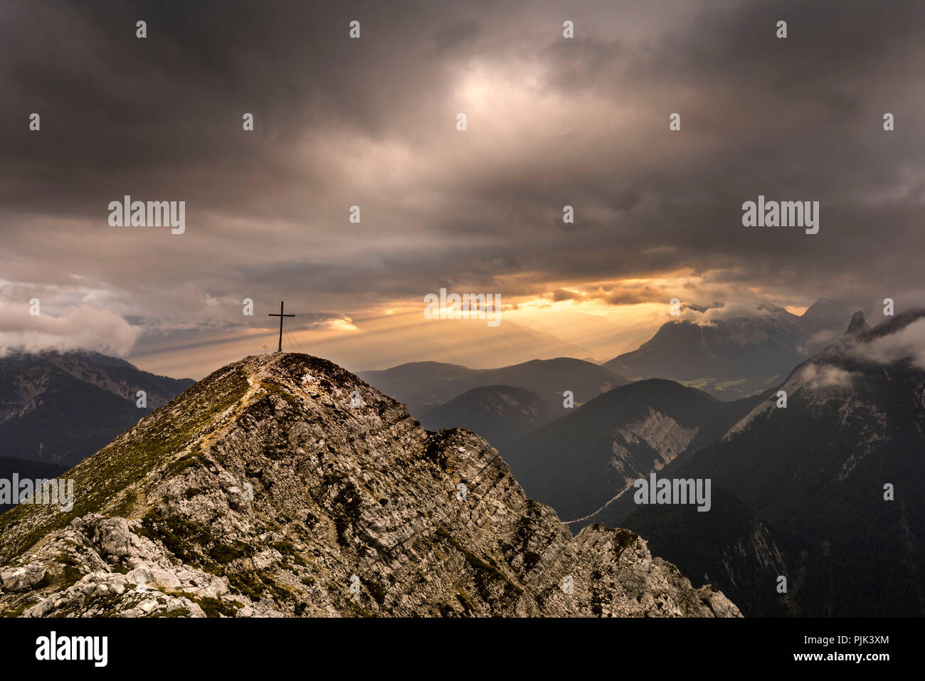 Gipfel der Brunnsteinspitze (2179 m) mit Gipfelkreuz und im Hintergrund Licht Stimmung in Tirol, von dramatischen Cloud Atmosphäre gerahmt, Stockfoto