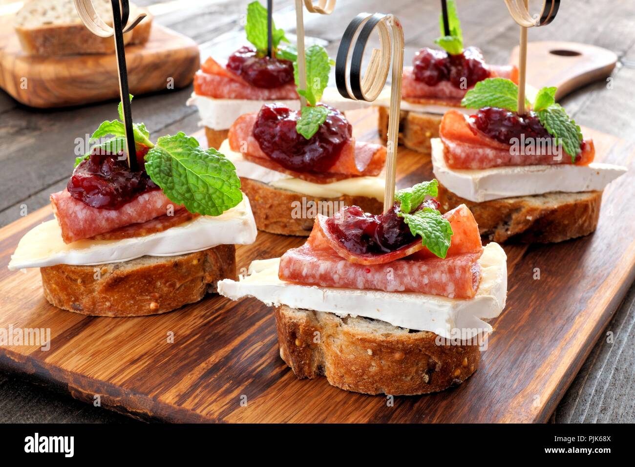 Urlaub crostini Vorspeise mit Preiselbeersoße, Brie, Salami und Minze auf einer hölzernen Server Stockfoto
