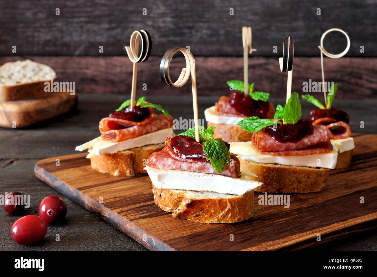 Urlaub crostini Spieße mit Preiselbeersoße, Brie, Salami und Minze auf einer hölzernen Server Stockfoto