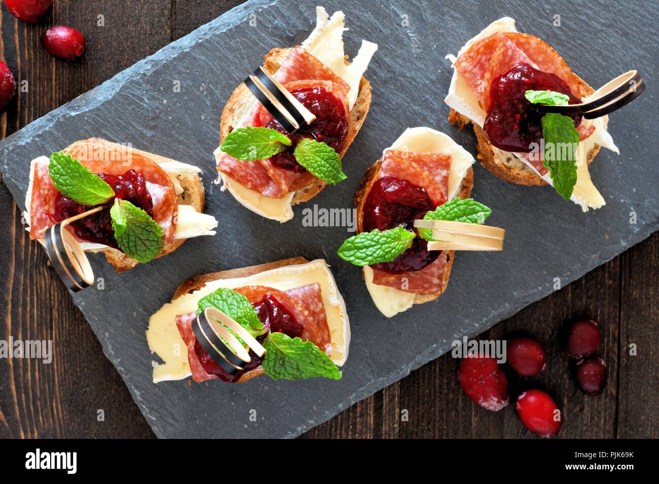 Urlaub crostini Vorspeise mit Preiselbeersoße, Brie, Salami und Minze oben Blick auf einer Schiefertafel server Stockfoto
