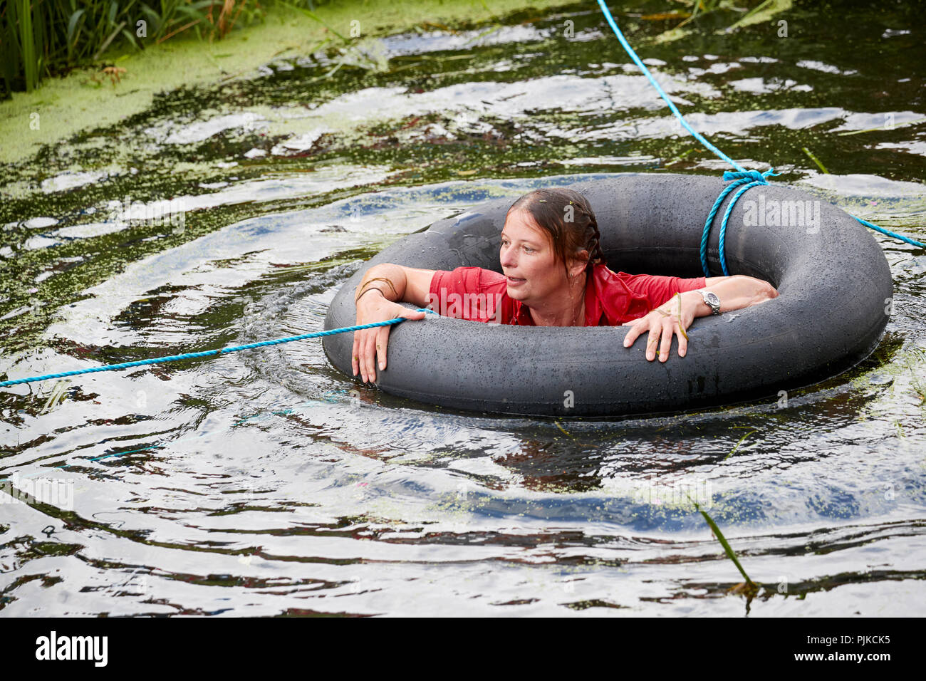 Frau in rot t-shirt Festhalten an einer inneren Rohr im Wasser auf einem Parcours im Tiefland Spiele, Thorney, Somerset, England Stockfoto