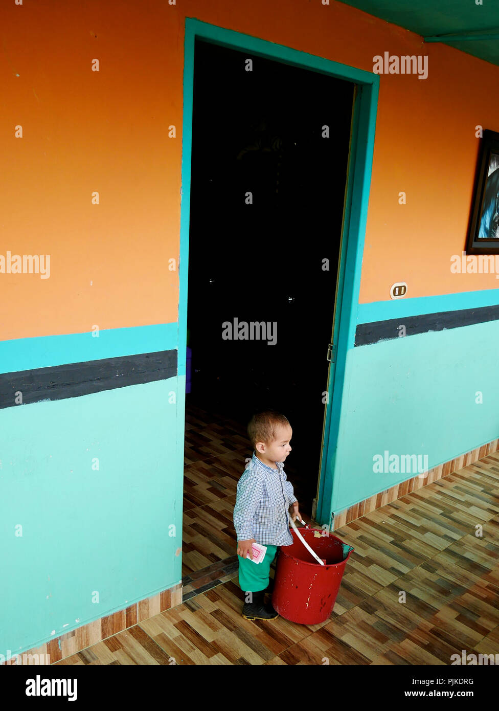 Ein kleiner armer Junge stand in der Tür seines Hauses mit einem roten Plastikeimer während einer katholischen Mission in der Heiligen Woche in der Stadt Jardín Kolumbien Stockfoto