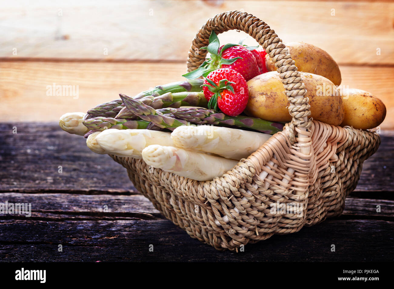 Spargel, Erdbeeren und Kartoffeln im Warenkorb auf Holz Stockfoto