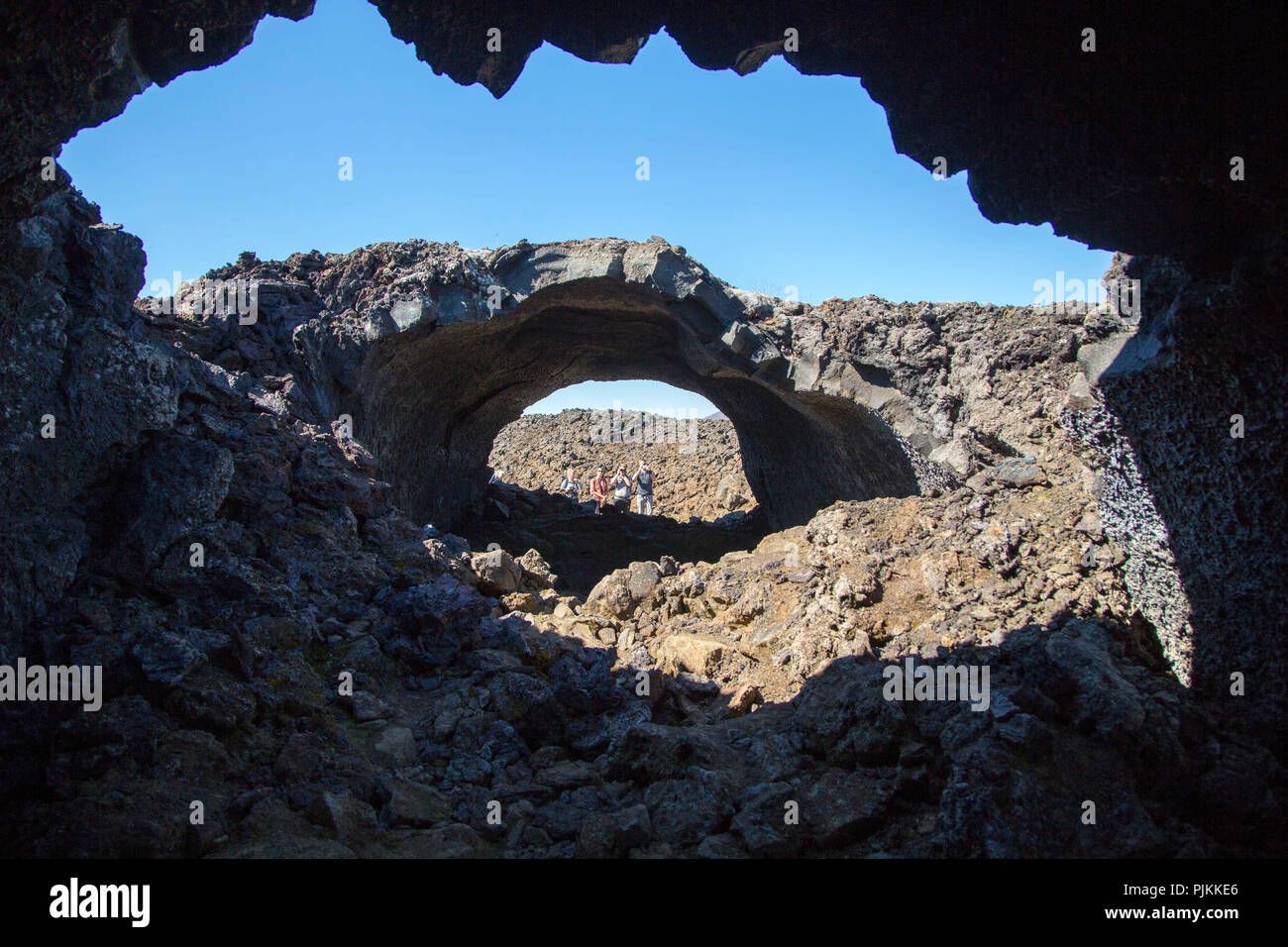 Island, Krafla Vulkan, Lava Tunnel in der Krafla Caldera, Wanderer im Hintergrund, blauer Himmel Stockfoto