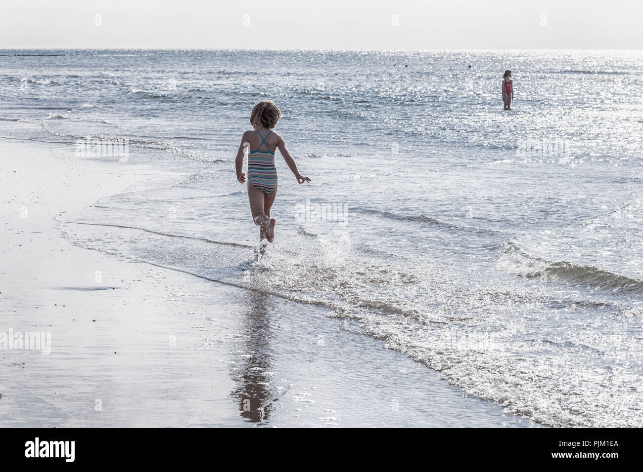 Mädchen läuft auf dem einsamen Strand, der durch das Wasser Stockfoto