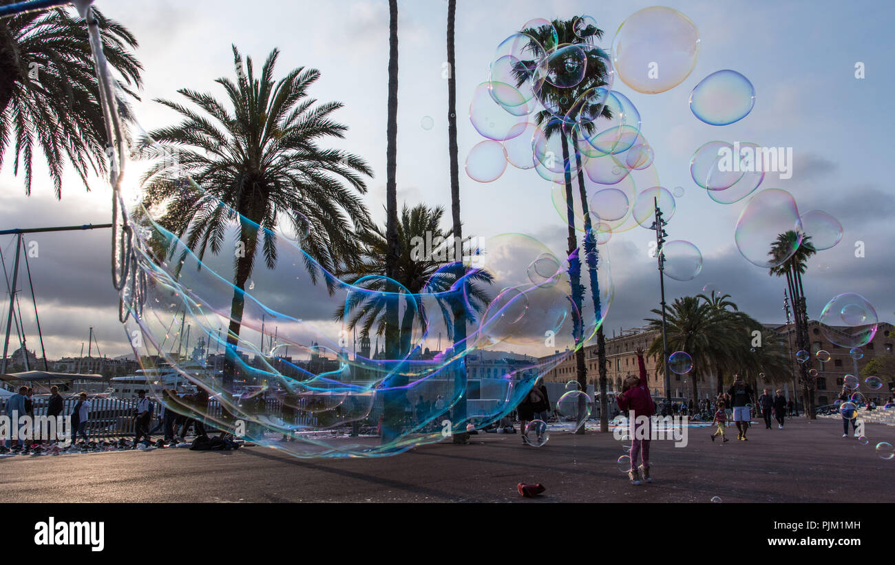 Street artist oder Bubble artist in Port Vell, Barcelona. Kleines Mädchen streckt und versucht die Blasen zu fangen Stockfoto