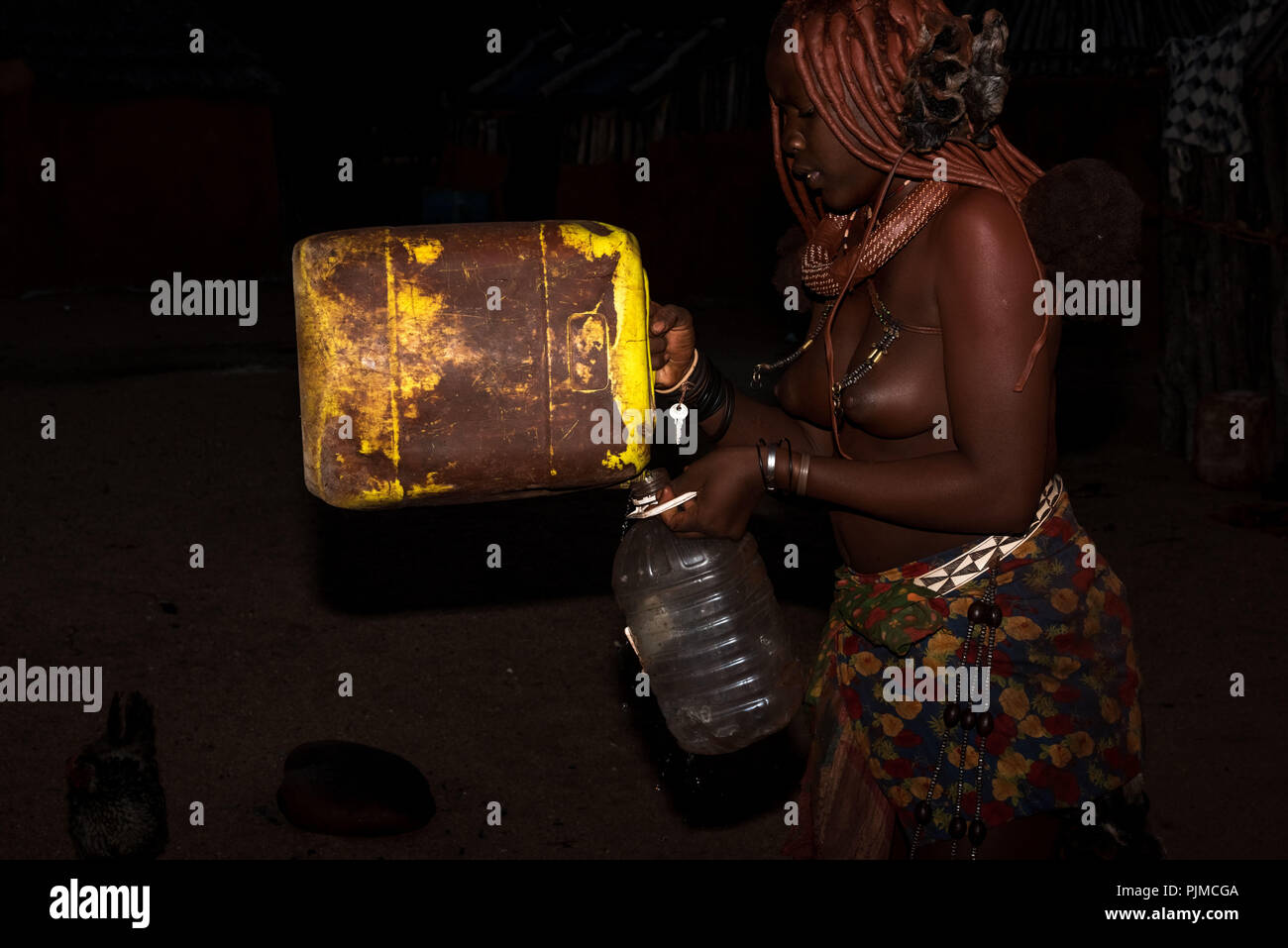 Junge Frau Himba gießen gesammelte Regenwasser, eine Seltenheit in Namibia, von einem Behälter in einer Kunststoffflasche Stockfoto