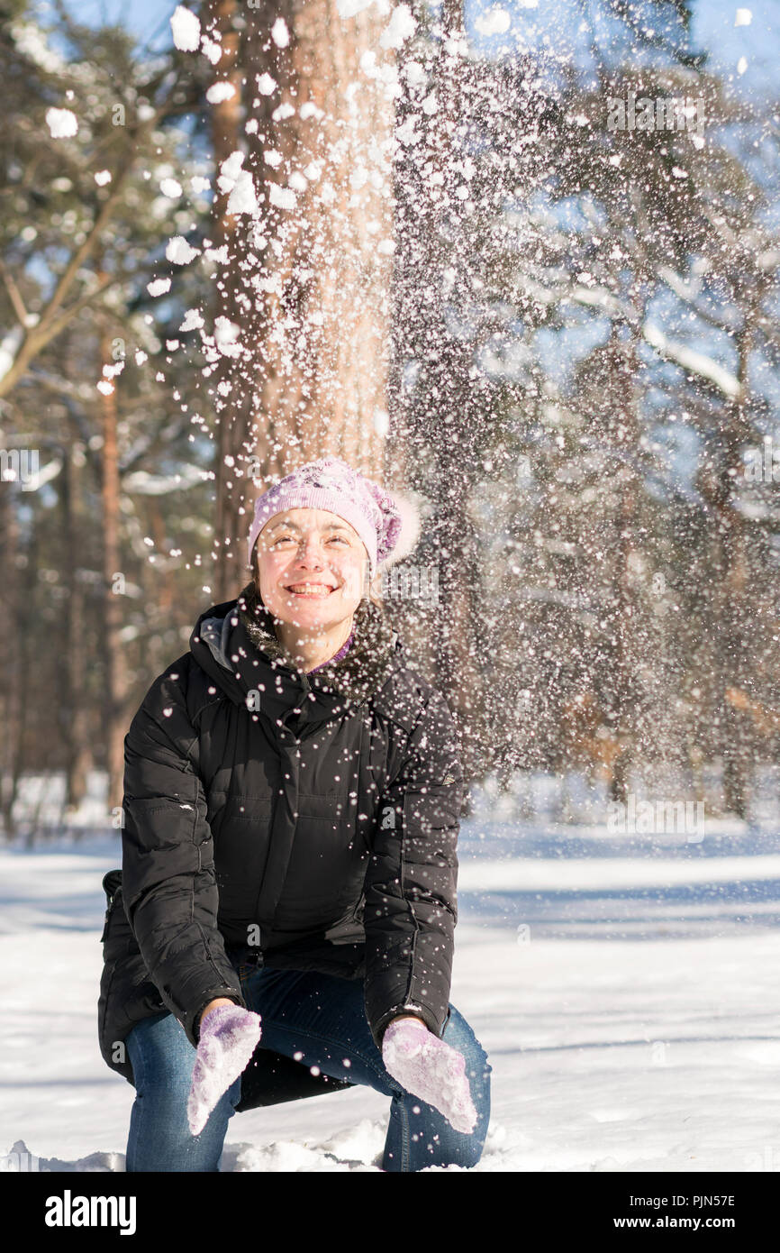 Mädchen wirft Schnee. Porträt der schönen Mädchen werfen Schnee im Winter. Glückliche junge Frau spielt mit einem Schnee im sonnigen Wintertag. Vertikale pho Stockfoto