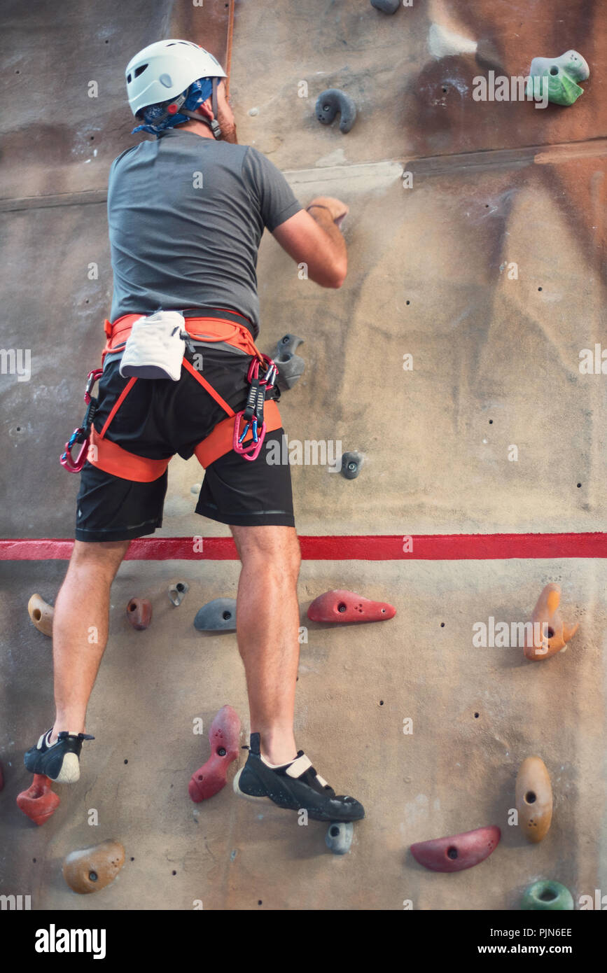 Junger Mann üben Klettern an künstlichen Wänden im Innenbereich. Stockfoto