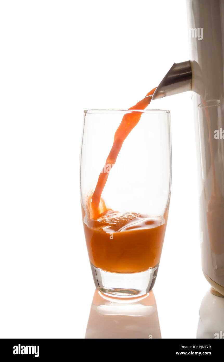Ein Glas frisch gepresster Karottensaft mit einem Entsafter. Auf einem weißen Hintergrund. Stockfoto