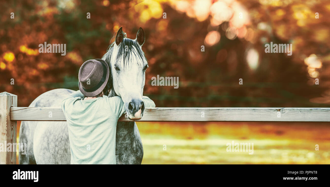 Kerl seinen Kopf in den Nacken des Pferdes am Zaun in stabilen auf dem Hintergrund von Herbstlaub Stockfoto