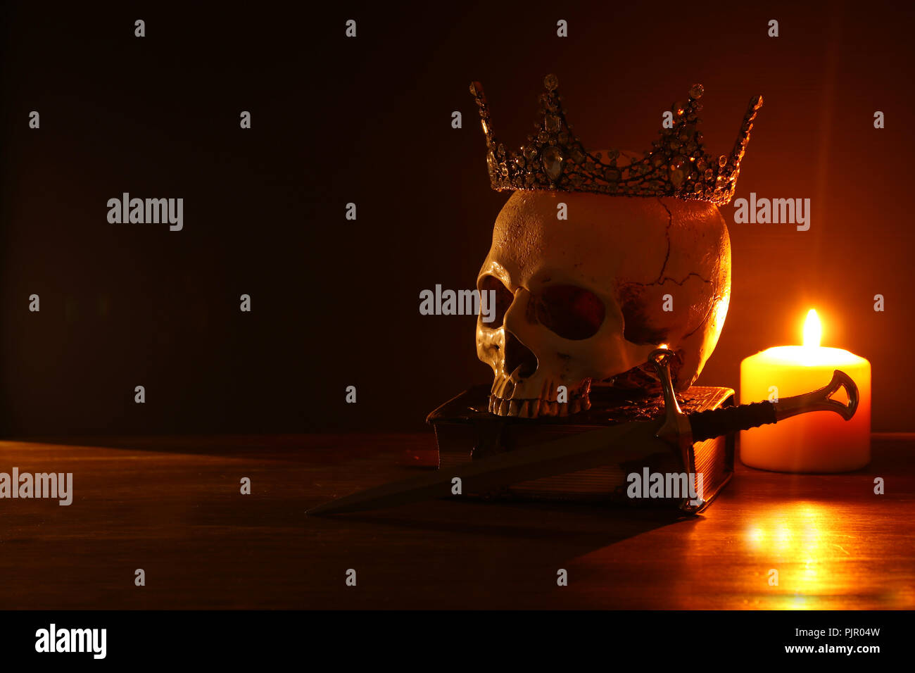 Menschlicher Schädel, altes Buch, Schwert, Krone und der brennenden Kerze über alten Holztisch und darl Hintergrund Stockfoto
