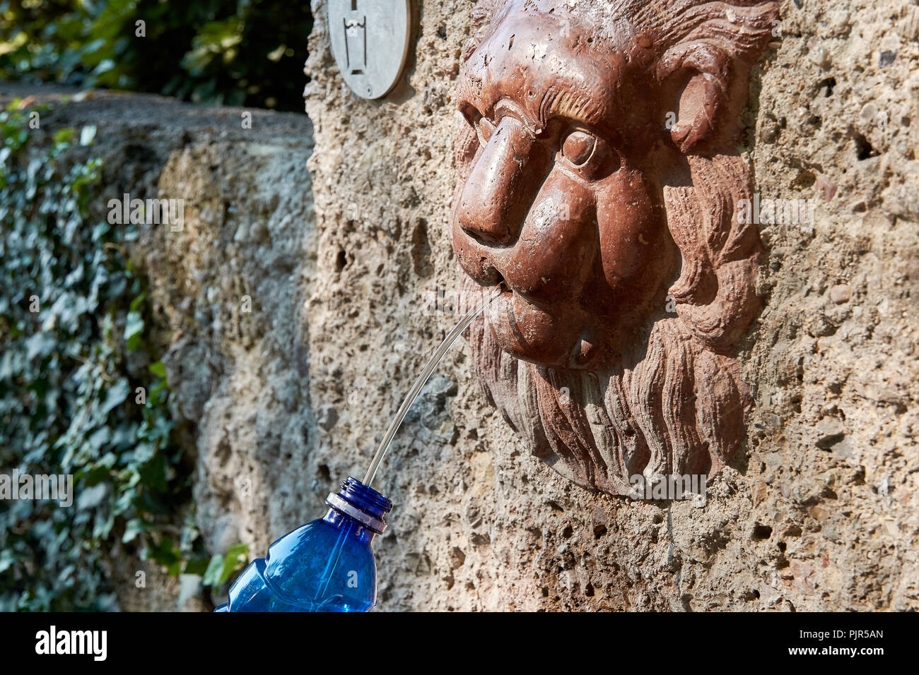 Eine detaillierte Ansicht eines Bronze Brunnen mit fließendem Wasser in Salzburg und einem blauen Kunststoff Flasche - Österreich in Europa Stockfoto
