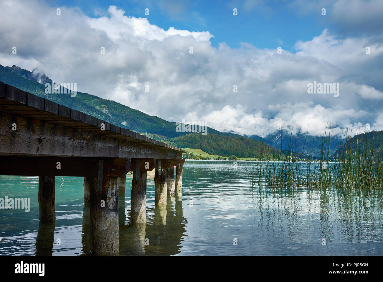 Blick auf den See in der Nähe von St. Wolfgang mit einem hölzernen Pier und Alpen Hintergrund, unter einem blauen Himmel mit Wolken an einem sonnigen Tag Stockfoto