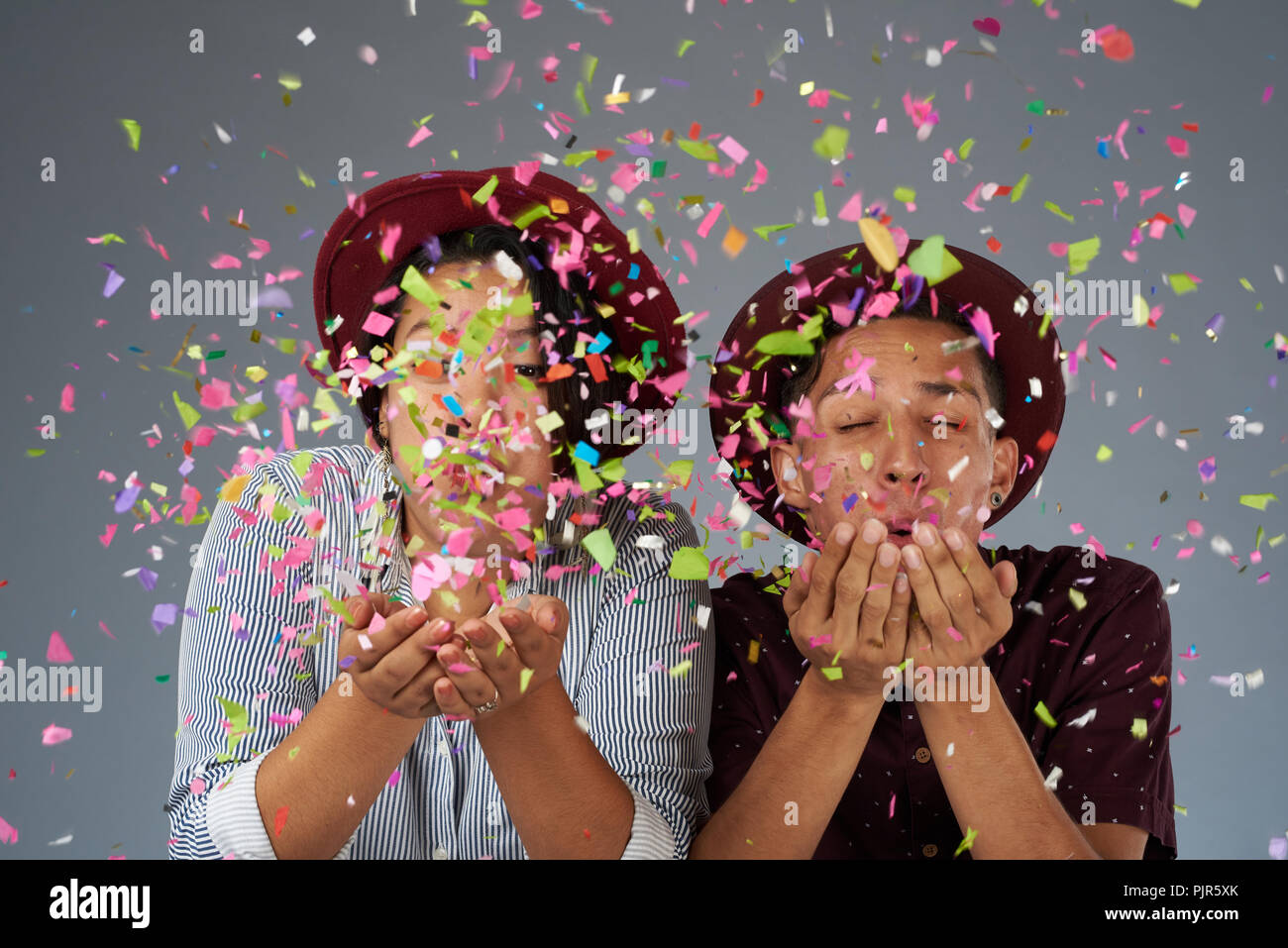 Junge Frau und Mann Schlag Konfetti in Grau studio Hintergrund Stockfoto