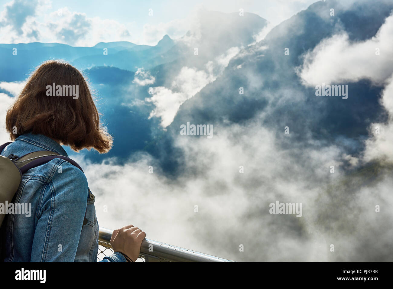 Eine junge Frau mit einem Rucksack durch das Geländer auf die Berge mit Wolken und Nebel den Blick in das Tal von Hallstatt. Österreich in der EU Stockfoto