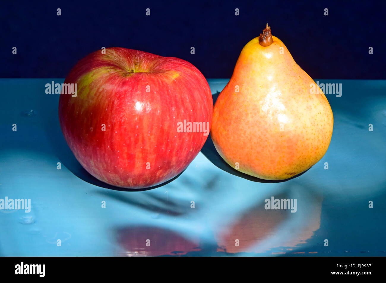 Ein Streifen roter Apfel und eine Gelbe Birne auf einer blauen Tabelle auf blauem Hintergrund in Nahaufnahme laterale Ansicht Stockfoto