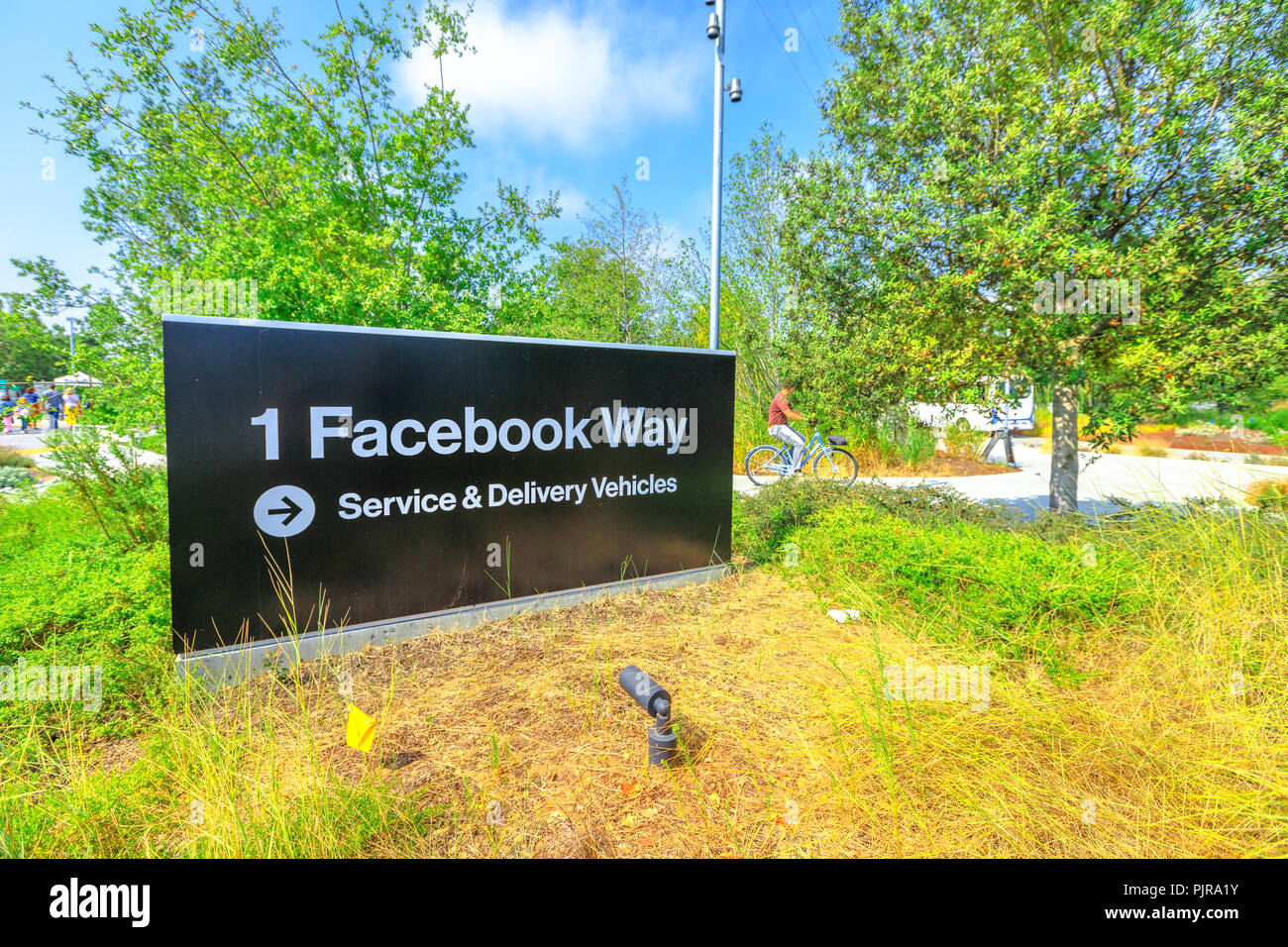 Menlo Park, Kalifornien, USA - 13. August 2018: Facebook HQ Eingang am neuen Campus im Silicon Valley. Im Hintergrund eine junge Mitarbeiterin geht mit der Firma Fahrrad zur Arbeit. Stockfoto