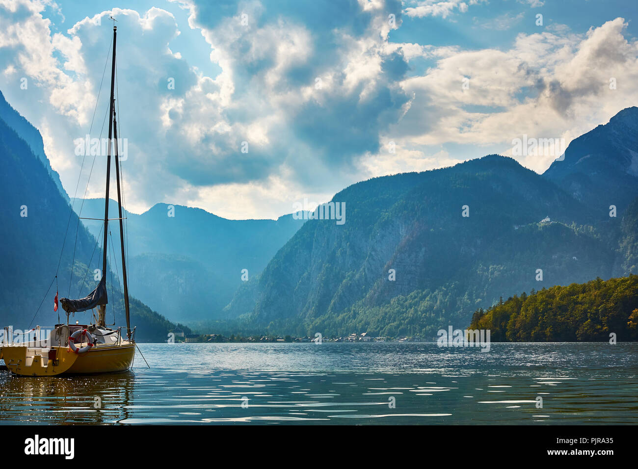 Ein Blick auf den Hallstätter See mit einer Yacht und Berge mit einem Wald im Hintergrund, unter einem blauen Himmel mit dramatischen Wolken. Österreich in Europa Stockfoto
