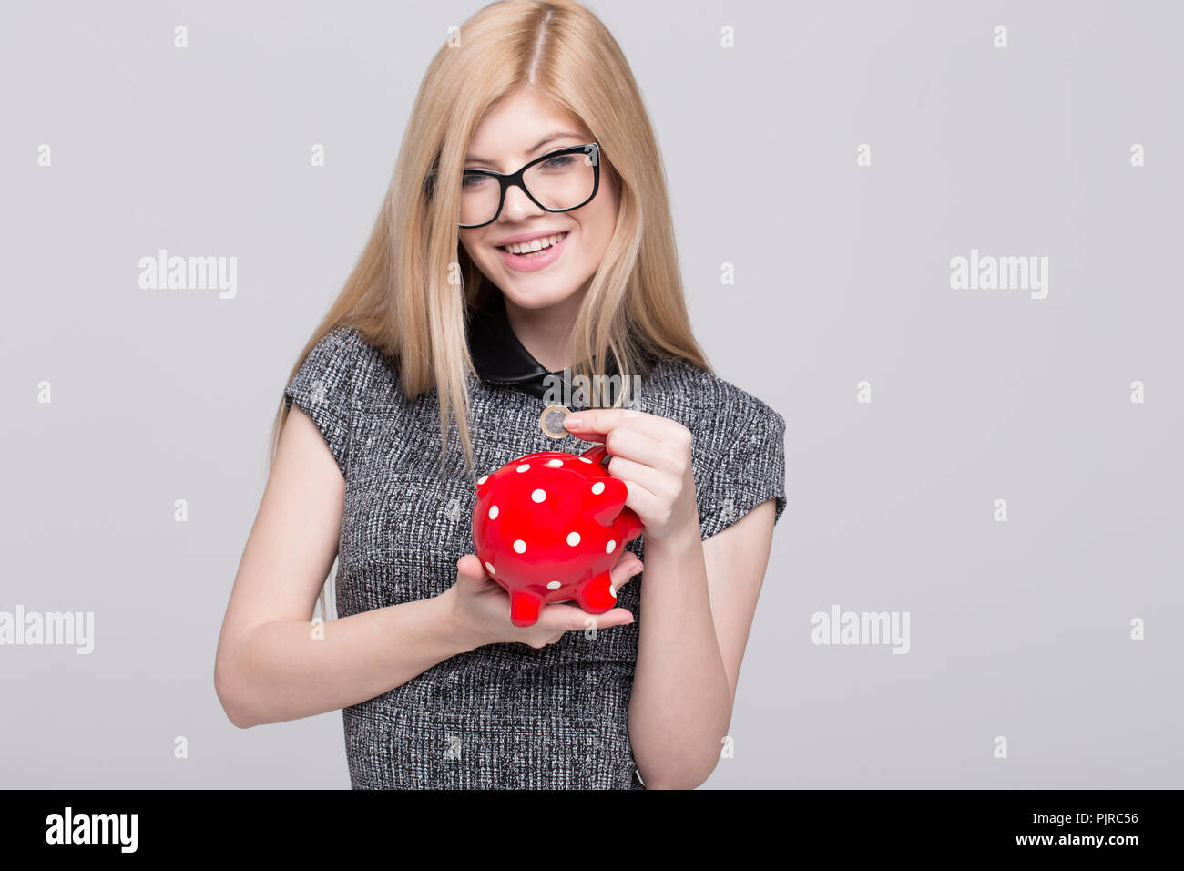 Junge Geschäftsfrau Drop 1 Euro Münze in Sparschwein, isoliert auf weißem Stockfoto