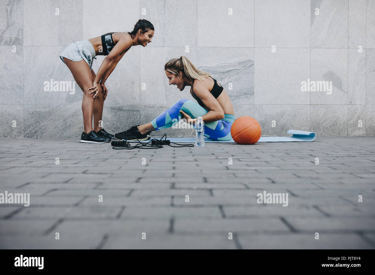 Seitenansicht der Frau tun, Sit Ups, während ihr Freund entspannt mit den Händen auf den Knien. Zwei fitness Frauen in fröhliche Stimmung beim Training im Freien. Stockfoto