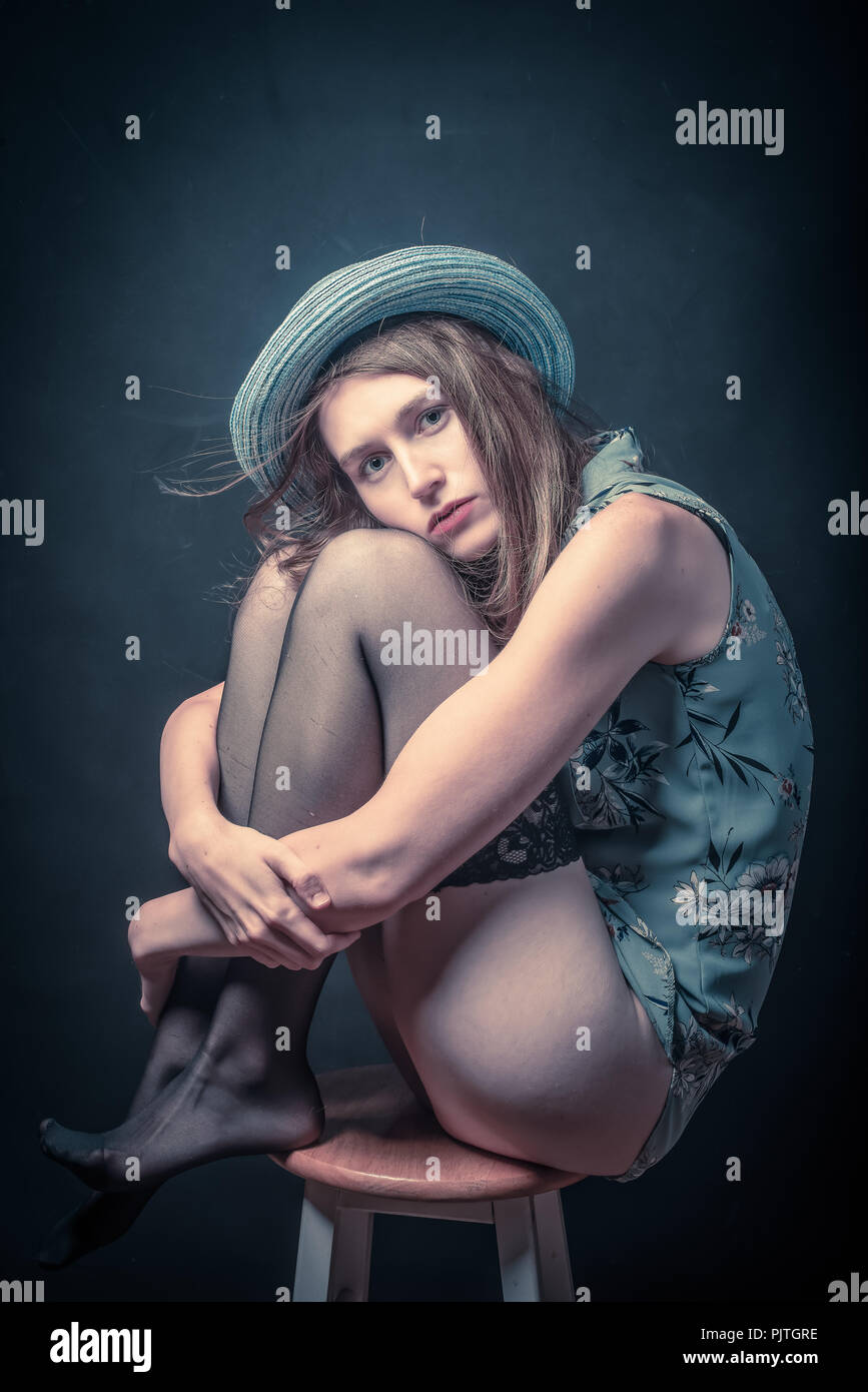 Studio Bild einer jungen Frau auf einem Hocker ihre Knie umarmt in einer depressiven Stimmung sitzen Stockfoto