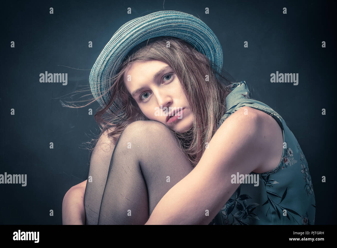 Studio Bild einer jungen Frau auf einem Hocker ihre Knie umarmt in einer depressiven Stimmung sitzen Stockfoto