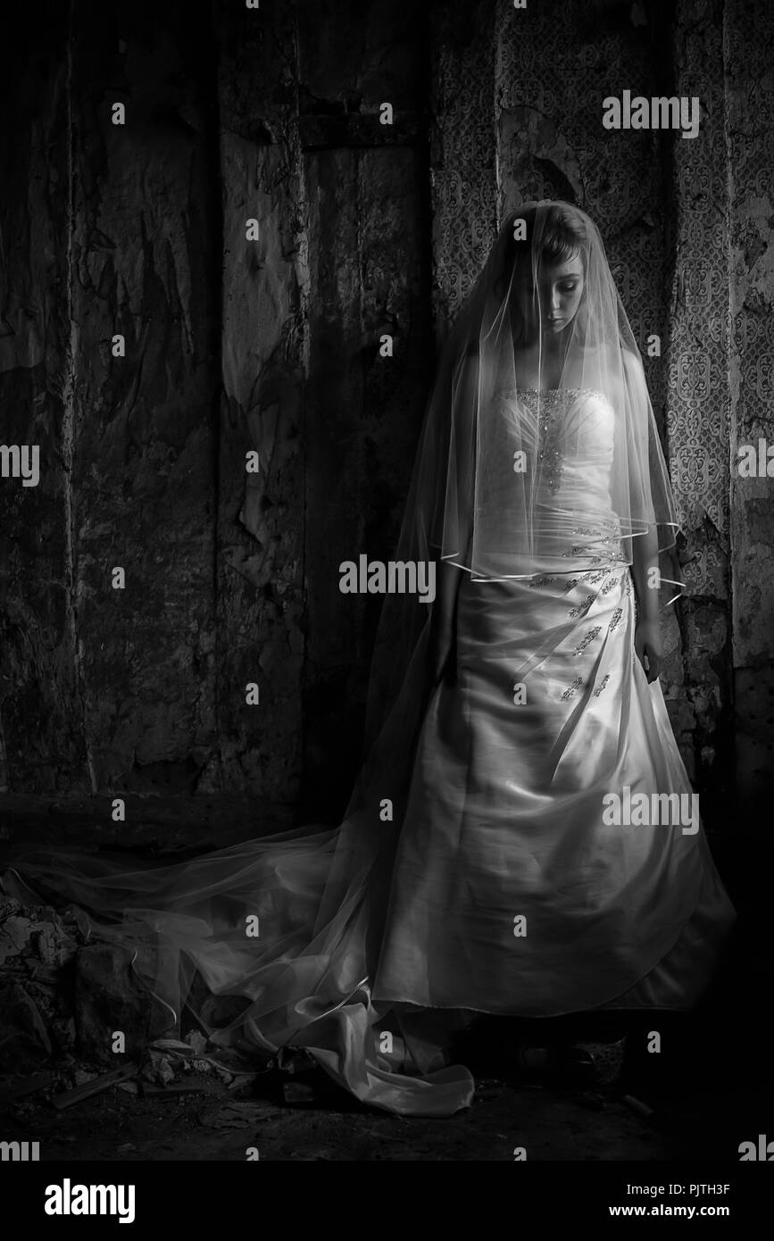 Eine Braut steht in ihrem Hochzeit Kleid und Schleier auf dem Boden in einem verlassenen Haus suchen. Stockfoto