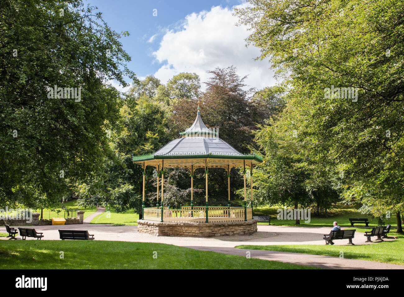 Hexham, Northumberland. Ein musikpavillon mit kunstvollen Schmiedearbeiten und ein spitzes Dach steht durch einen Pfad und Bänken umgeben. Es ist von alten Bäumen eingerahmt. Stockfoto