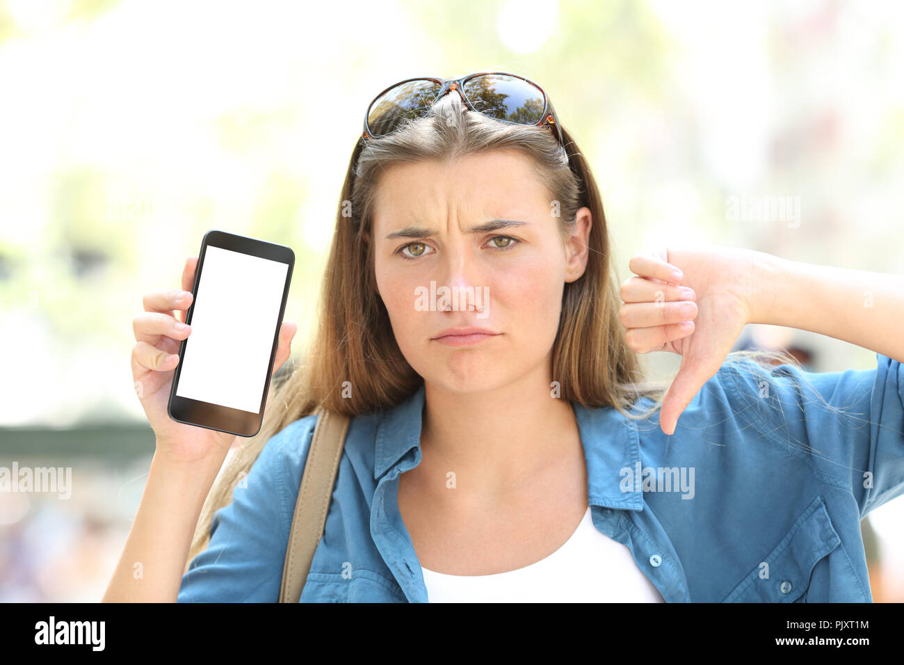 Vorderansicht Porträt eines zornigen Mädchen zeigt leeren Bildschirm "Telefon" mit dem Daumen nach unten auf der Straße Stockfoto