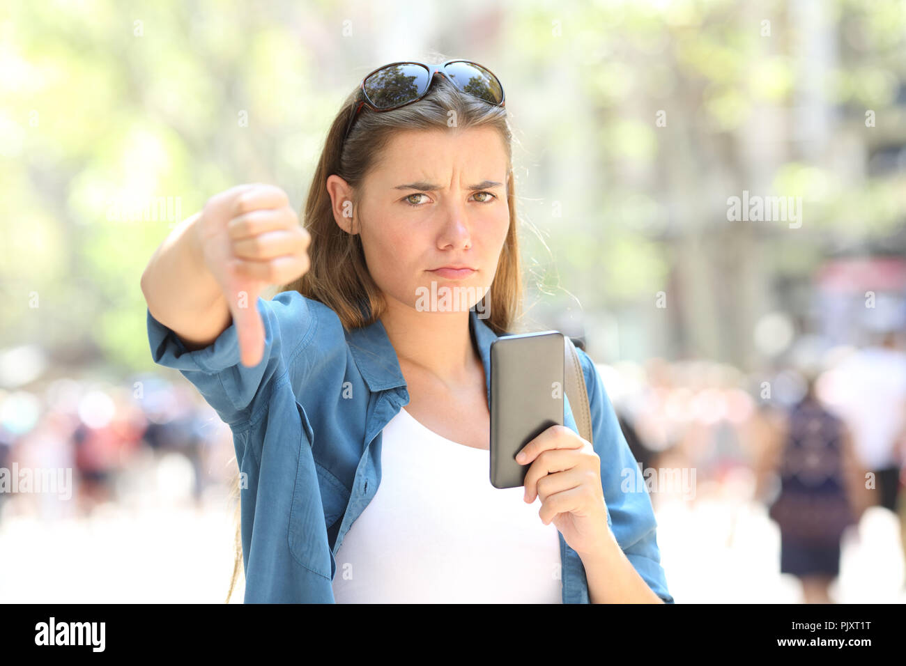 Verärgert Frau ein smart phone an Kamera suchen mit Daumen gedrückt halten auf der Straße Stockfoto