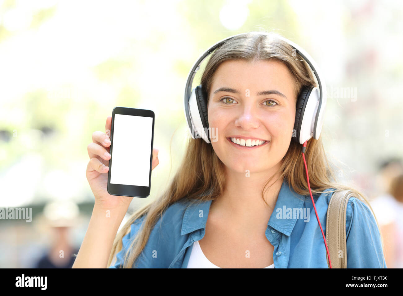 Vorderansicht Portrait eines glücklichen Mädchen mit Kopfhörer, leere Smart Phone screen auf der Straße Stockfoto