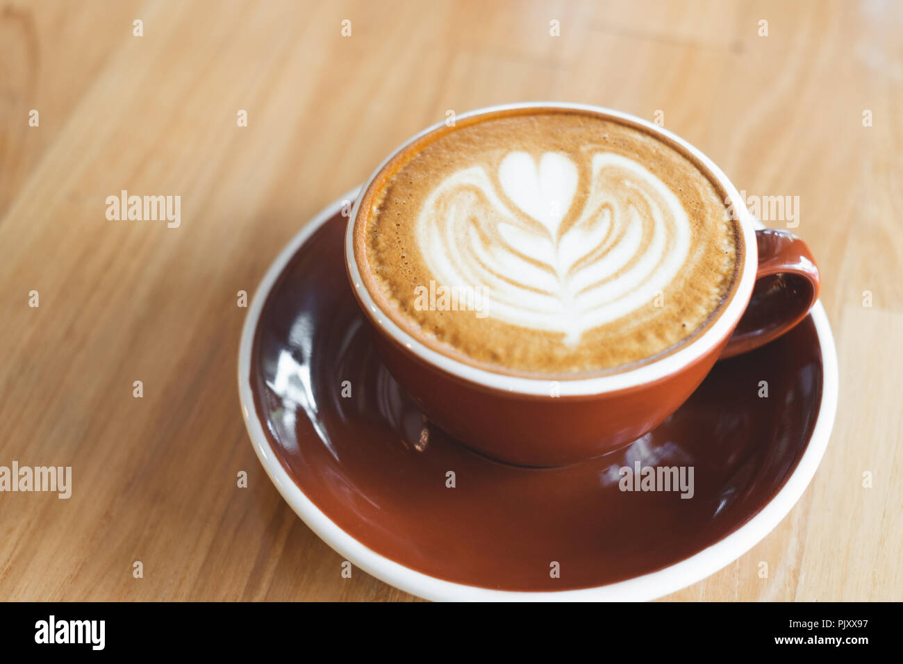 Close up heißen Cappuccino rot Kaffeetasse mit Herzform latte Kunst auf Holz Tisch im Cafe, Drak Tone Filter, Essen und Trinken Stockfoto