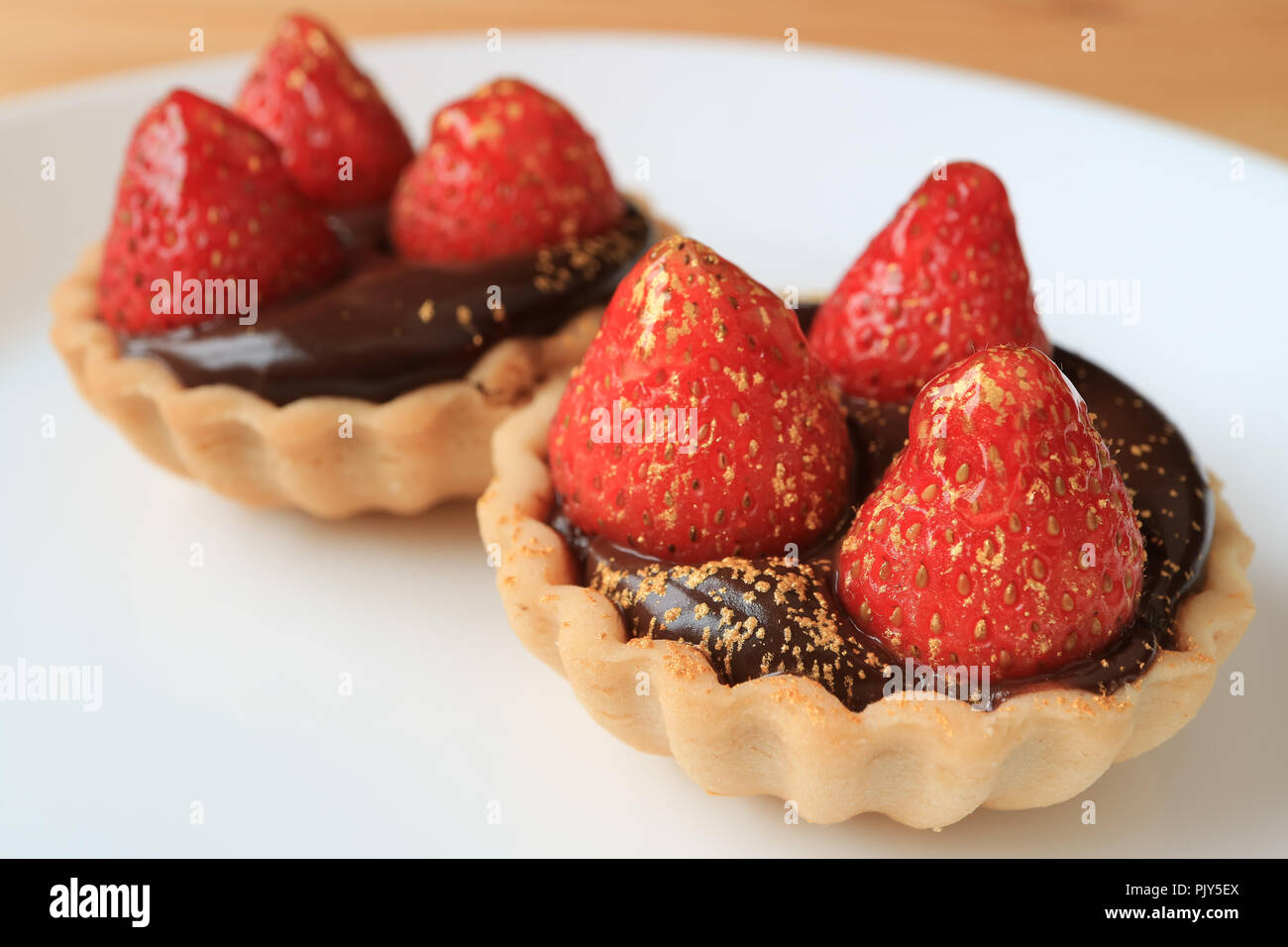 Paar Schokolade Torten gekrönt mit frischen Erdbeeren und genießbare gold Pulver serviert auf weiße Platte Stockfoto