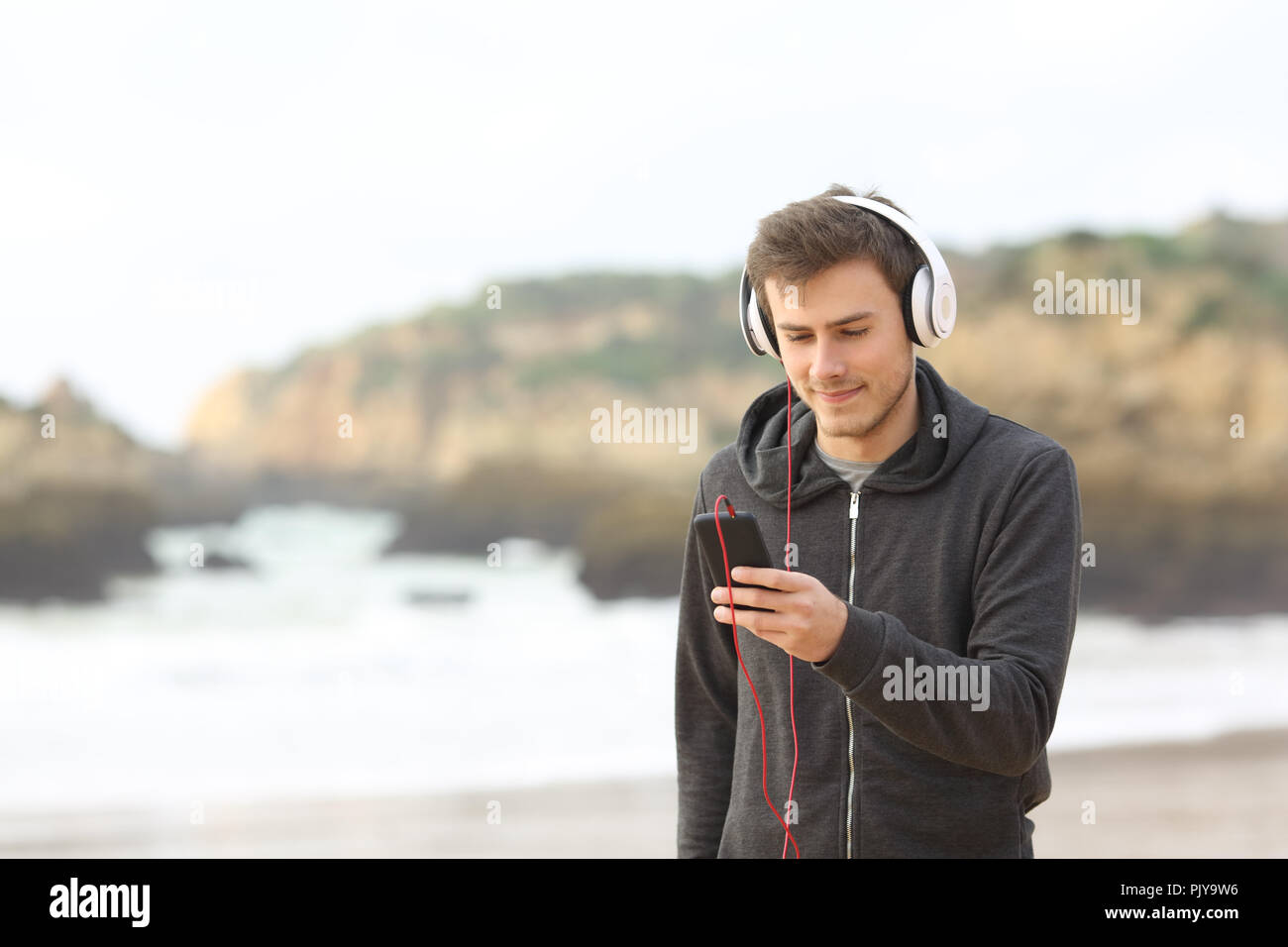 Jugendlich entspannt Musik hören mit Kopfhörern und ein Smart Phone zu Fuß am Strand Stockfoto