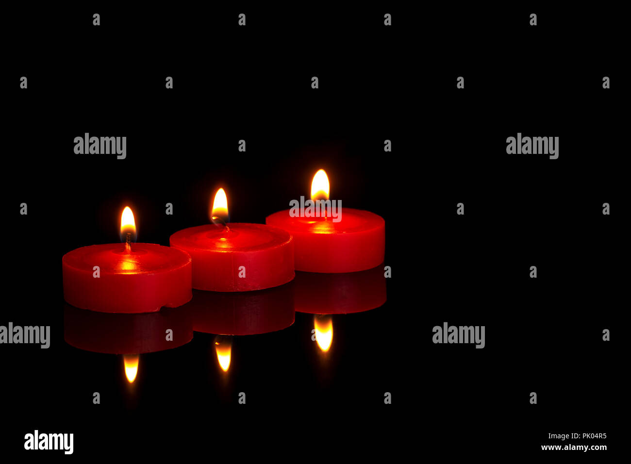 Drei kleine rote Kerzen, Teelichter, Brennen in der Nacht auf Schwarz. In memoriam oder religiösen vielleicht. Stockfoto