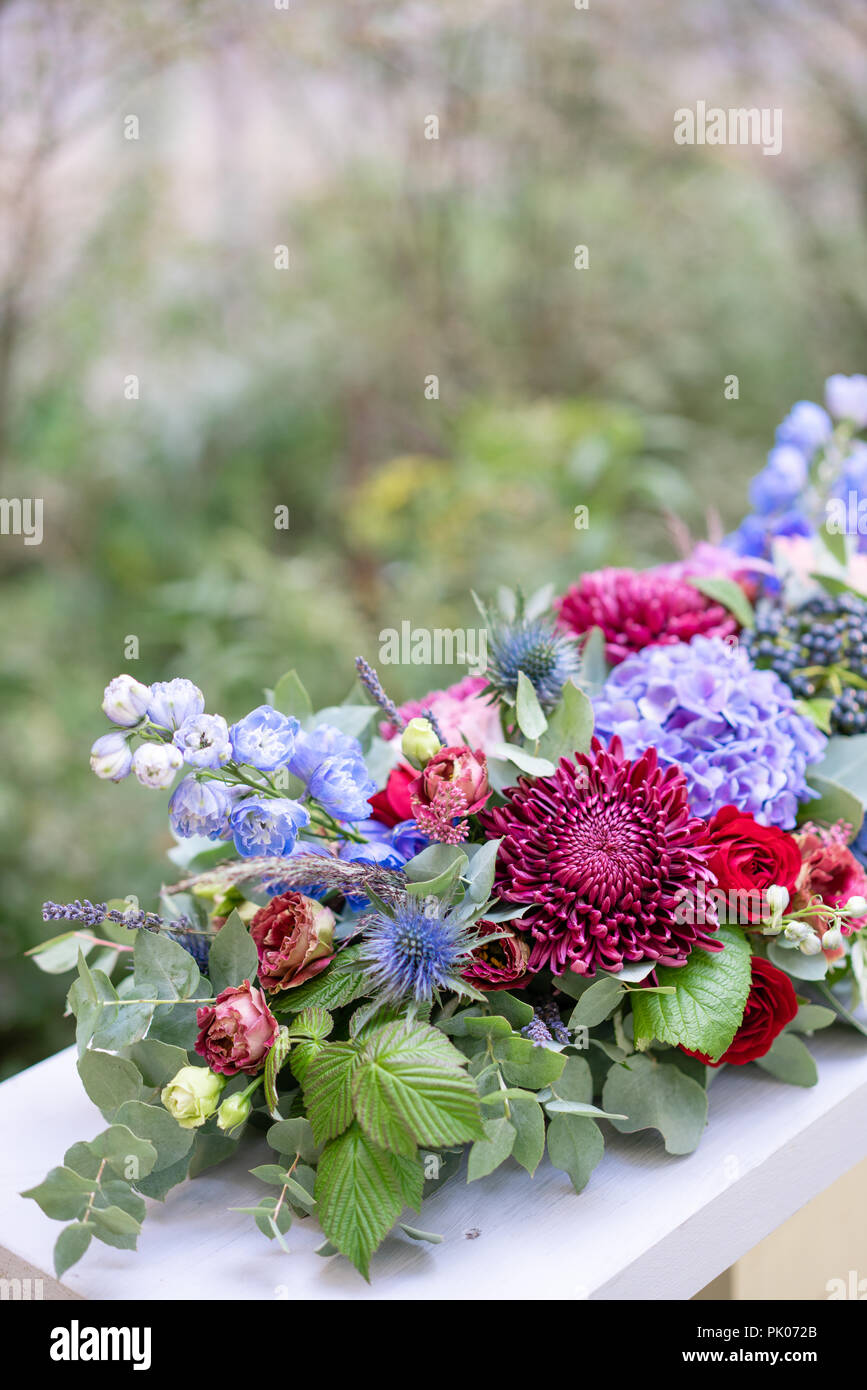 Längliche Blumenschmuck in Vintage metall Vase. Tabelle einstellen. Blaue und rote Farbe. Wunderschönen Blumenstrauß aus verschiedenen Blumen. Park auf Hintergrund Stockfoto