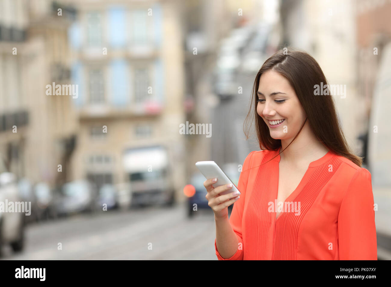 Glückliche Frau in orange verwendet ein Smart Phone zu Fuß auf der Straße Stockfoto