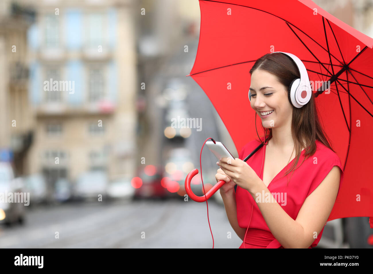 Glückliche Frau Hören von Musik mit Telefon und Kopfhörer an einem regnerischen Tag in der Straße Stockfoto