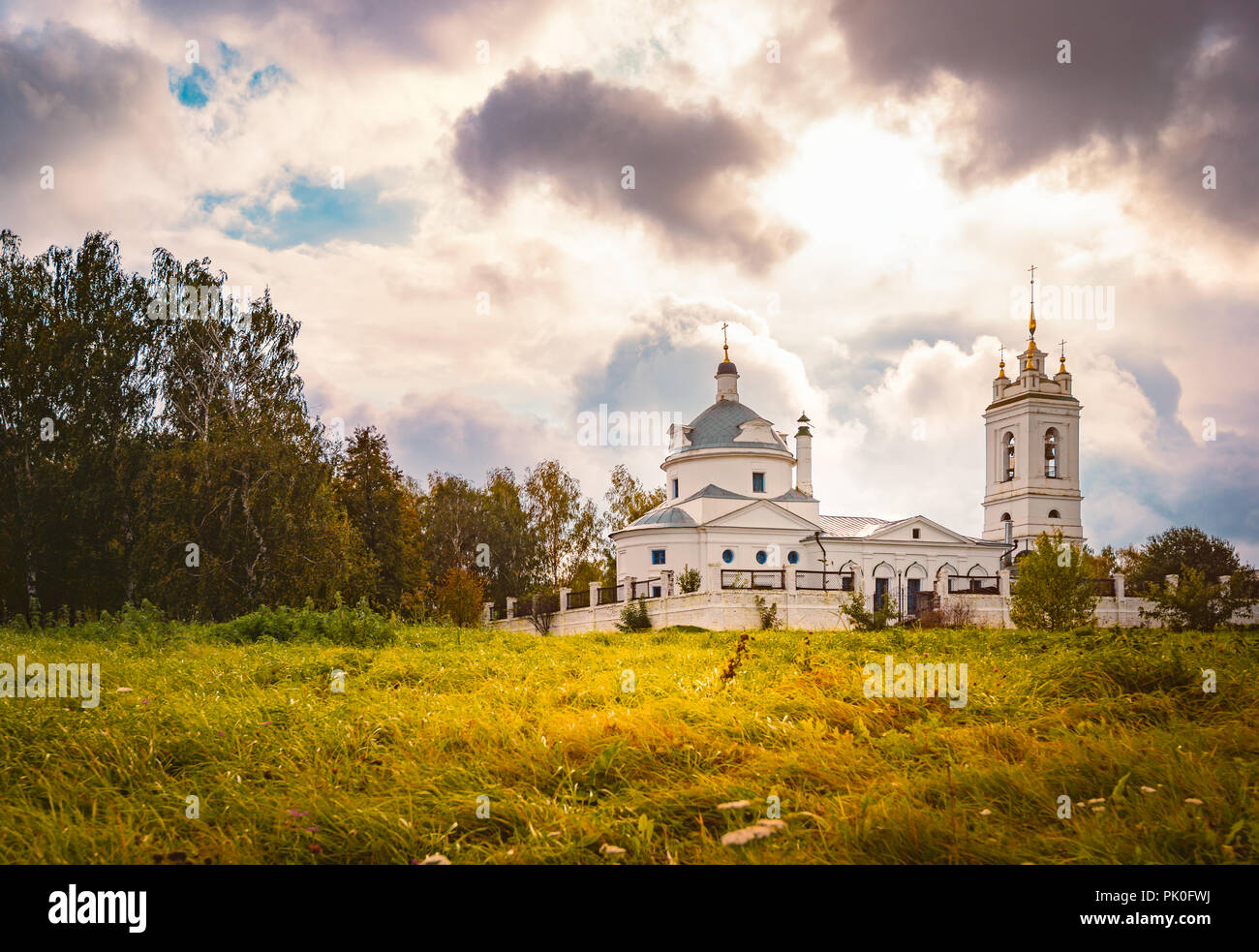 Kirche in Konstantinovo, Moskau, Russland. Dramatischer Sonnenuntergang bewölkter Himmel im Hintergrund und die Wiese im Vordergrund. Stockfoto