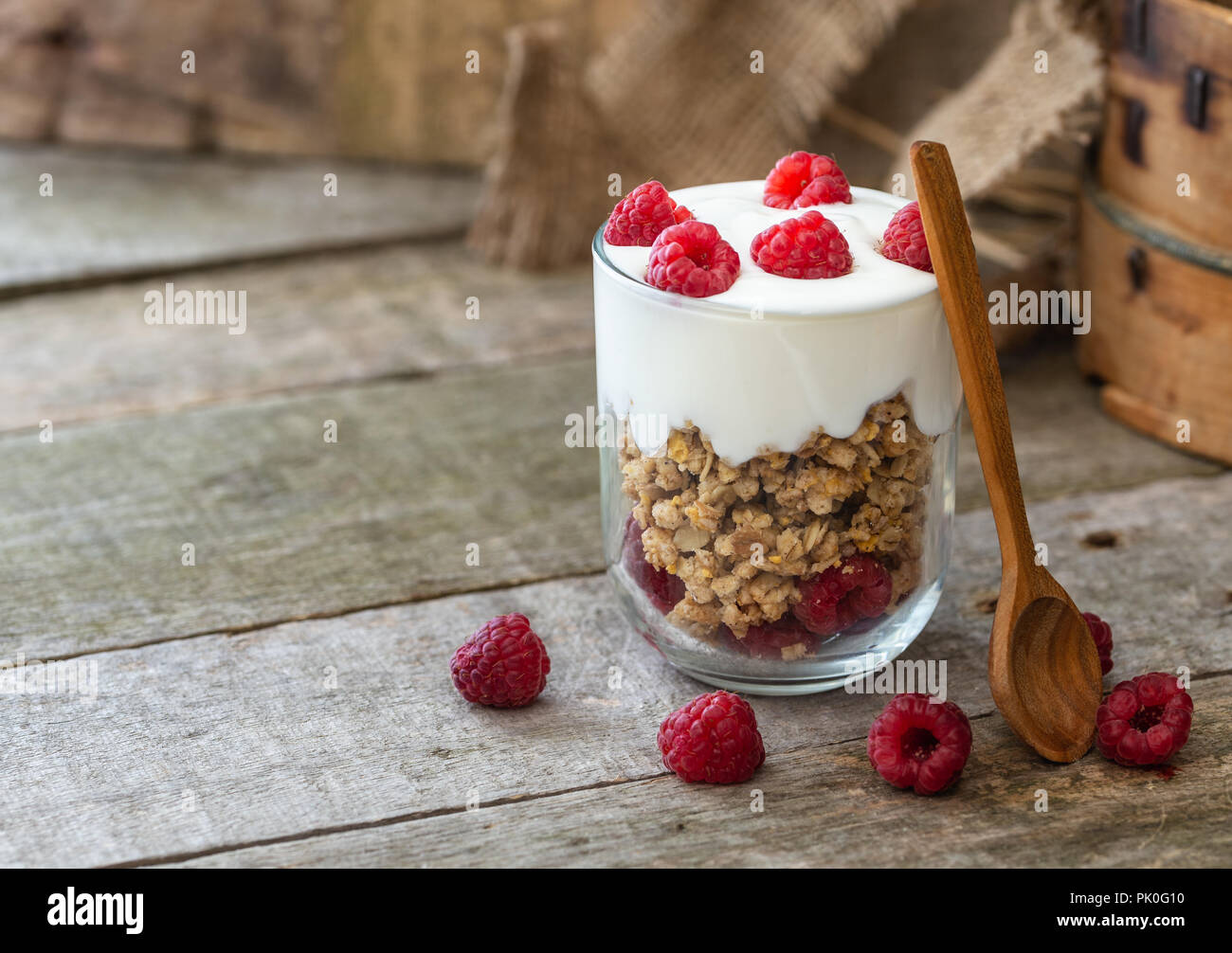 Weißer Joghurt mit Müsli in Glasschale mit Himbeeren auf natürliche Holzschreibtisch. Stockfoto